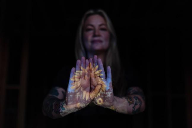 A photo of sunflowers Missi Dowd-Figueroa once grew on her property is projected onto her palms as she poses for a portrait at her rebuilding site in Altadena, California.