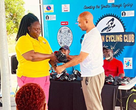 Elevation Cycling Club secretary Taneish Dixon (left) makes a symbolic presentation to Kevin Dillon of Dillies Cycle World during the ceremony at which 80 pairs of high-performance cycling shoes, valued at more than US$8,000, were donated to key cycling in