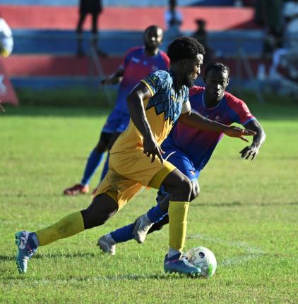 Racing United’s Marcovich Brown dribbles away from the pressure of Dunbeholden’s Ricardo Beckford during their Jamaica Premier League encounter at Ferdi Neita Park yesterday. The game ended 1-1.