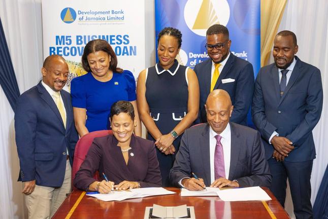 Gillian Hyde (front row left), deputy managing director, JN Bank, and Dr David Lowe, managing director, Development Bank of Jamaica (DBJ) sign a partnership agreement to help micro and small businesses affected by Hurricane Melissa to restore operations th