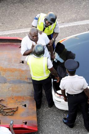 A man stands between his car and a wrecker to avoid the towing of his car in downtown Kingston in 2011. He was allegedly caught after being chased by the police and Transport Authority inspectors.