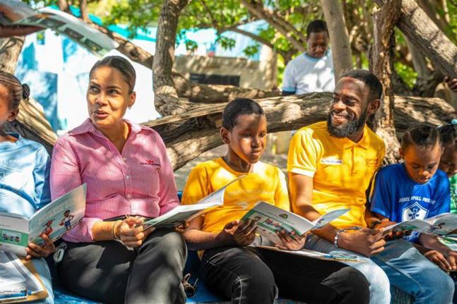 Gail Moss-Solomon, general counsel & chief corporate secretary (left) and Kenny-Dee Bryan, human resource officer, Consumer Brands Limited, and GK Earth365 Ambassador (second right) join students from the Jessie Ripoll Primary School in a read-aloud of the