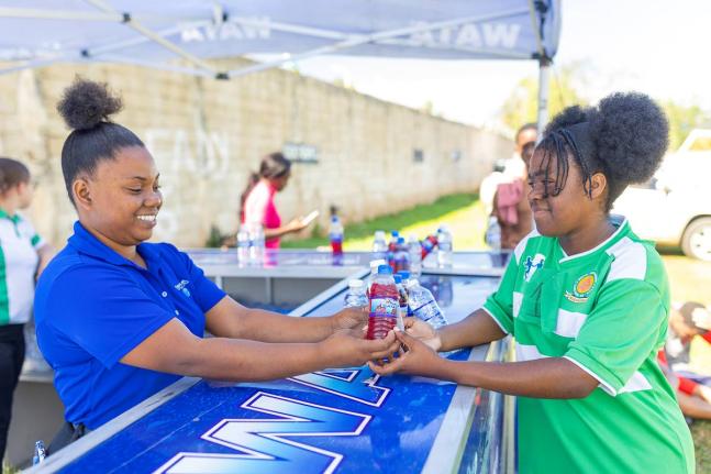 Savana Clarke (left), WATA brand representative, hands a chilled bottle of water to Rushawna Ebanks at the hydration station during WATA’s Hydrate to Educate School Tour stop at BB Coke High School in St Elizabeth on Wednesday, March 5. The visit formed 